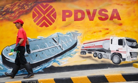 A worker walks past a mural with a PDVSA logo at a petrol station in Caracas