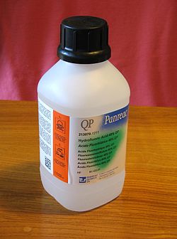 White plastic bottle with safety cap is labeled "QP Panreac" above smaller text "Hydrofloric Acid 40% QP" with 6 translations. In a bright orange region along the side, warning symbols are clearly visible.