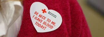 A woman wearing a sticker that says "Be nice to me, I gave blood today!"