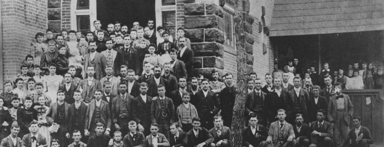 The 1894 student body seated on the steps of the Normal Building, the first permanent university structure. This building was located at the corner of Hickory and Avenue B.