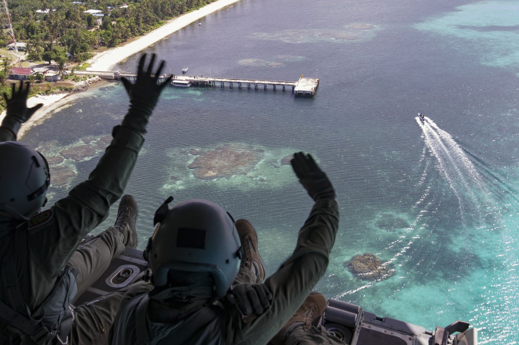 Airmen from Team Yokota and Andersen wave out the back of a C-130H Hercules to the people of Kayangel, Republic of Palau, Dec. 11, 2015, during Operation Christmas Drop. Every December, C-130H Hercules aircrews from Yokota head to Andersen Air Force Base to execute low-cost, low-altitude humanitarian airdrops to islanders throughout the Commonwealth of the Northern Marianas, Federated States of Micronesia, Republic of Palau. These islands are some of the most remote locations on the globe spanning a distance nearly as broad as the continental U.S. It is the longest-running Department of Defense humanitarian airdrop operation with 2015 being the first trilateral execution with support from Japan Air Self-Defense Force and Royal Australian Air Force. (U.S. Air Force photo by Osakabe Yasuo/Released)