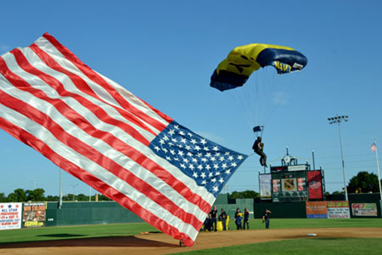 160719-N-WR119-494 A Sailor assigned to the Navy parachute demonstration team, the Leap Frogs, jumps with the American flag into Sioux Falls Stadium.