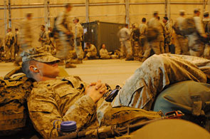 A service member sleeps against luggage on floor
