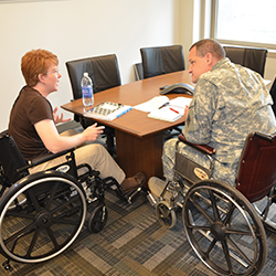 A woman and a service member in wheelchairs, meeting at a table