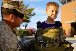 Service member helps five-year-old boy try on a flak jacket