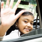 Young girl waving goodbye through open car window