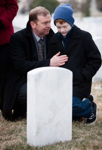 Brig. Gen. Richard Scobee and his son, Andrew, kneel near the grave of Dick Scobee earlier this year during the NASA Day of Remembrance. Dick Scobee was the commander of the Space Shuttle Challenger, which exploded shortly after launch in 1986. His grave is near the memorials to the Space Shuttles Challenger and Columbia in Arlington National Cemetery’s Section 46. (Courtesy photo)