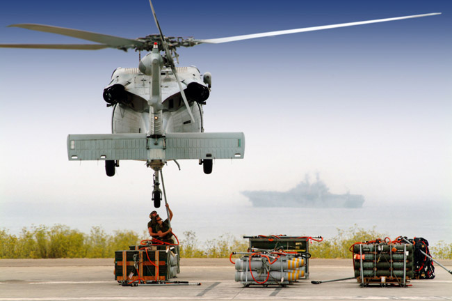 A MH-60S Seahawk helicopter is prepared to transport pallets of ammunition to an amphibious assault ship waiting off the coast. 