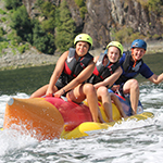 Three teenagers wearing life jackets and helmets on an inflatable water toy being pulled through the water