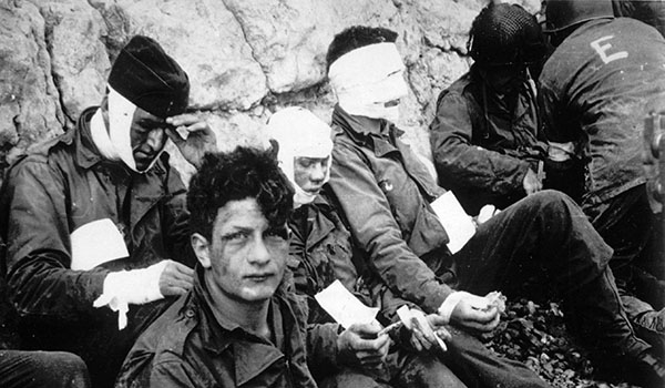 Soldiers of the Army’s 16th Infantry Regiment, wounded while storming Omaha Beach, wait by the chalk cliffs for evacuation to a field hospital for treatment after D-Day. Photo courtesy of Center of Military History 