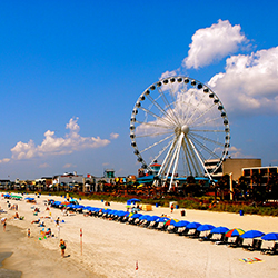 People-filled beach with Ferris wheel and hotels. 