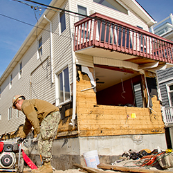 Service members starting a generator next to a home damaged by a storm