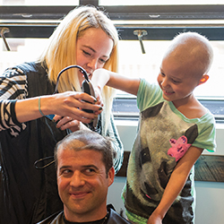 A mother and daughter shaving the hair off a man’s head