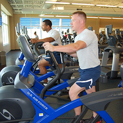 Two male airmen working out on elliptical machines 