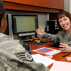 A female service member talking to another service member across a desk. 