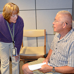 A woman leaning down to talk to an older man sitting in a chair