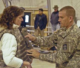 Man in military uniform helping woman put on body armor vest