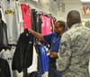 Man in civilian clothes holds up shirt on hanger while talking with Soldier in Exchange Service Store