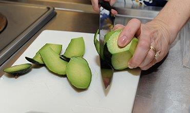 Photo: Hands cutting a piece of fruit on a cutting board.