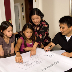 Mother, father and two daughters at the kitchen table reviewing a map of their house and their fire escape plans.