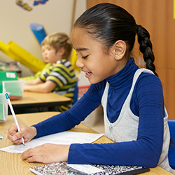 School-aged girl writing at a desk and smiling