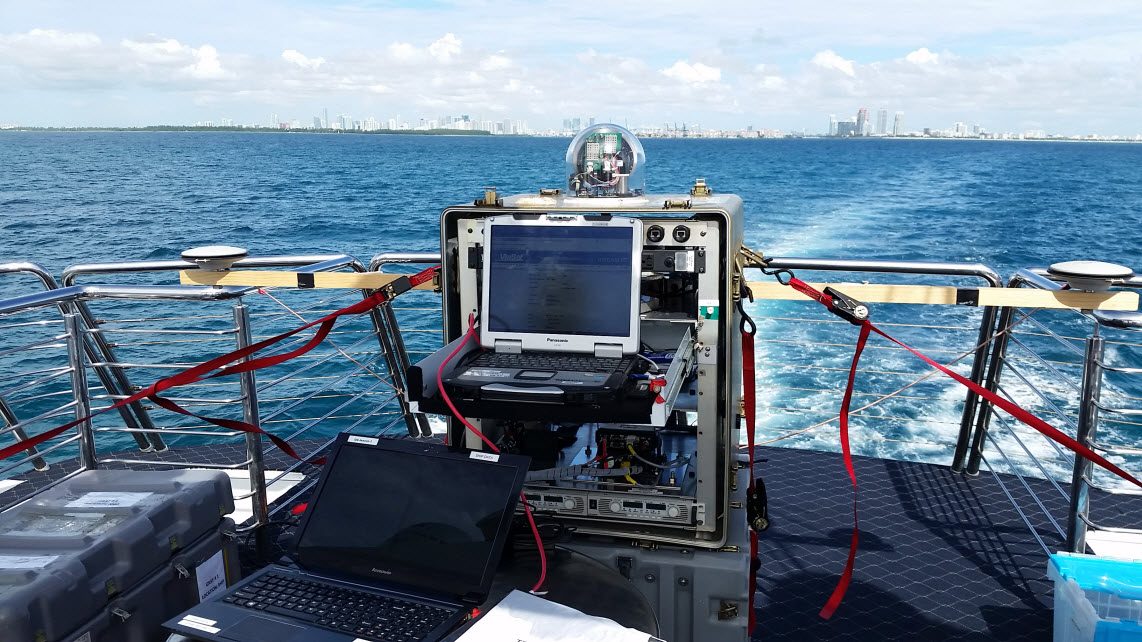 TREC test assembly shown on the charter vessel as it enters the Port of Miami. Researchers established communications links with a similar terminal located on the roof of one of the buildings in the distance. Photo by U.S. Naval Research Laboratory.