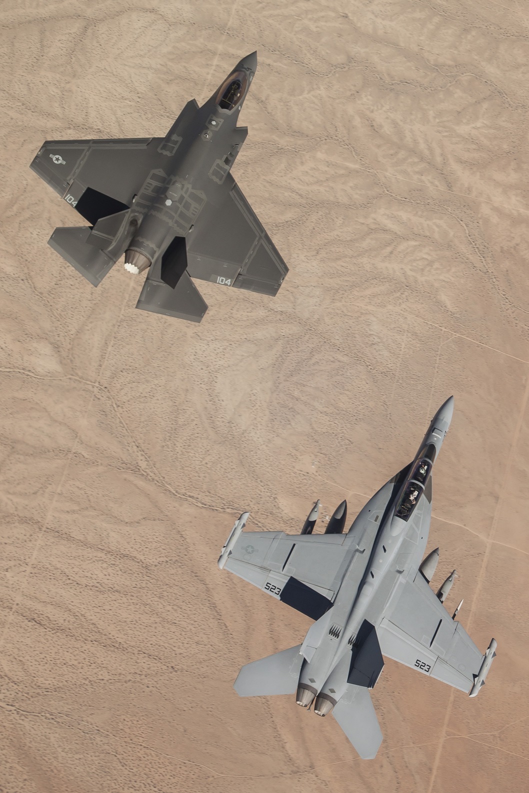 MOJAVE DESERT, Calif. (Aug. 28, 2014)  A U.S. Navy F/A-18F Super Hornet assigned to the Dust Devils of Air Test and Evaluation Squadron (VX) 31 at Naval Air Weapons Station China Lake, Calif., conducts an interoperability test event with a Navy F-35C Lightning II joint strike fighter aircraft over the Edwards Air Force Base test range with the Mojave Desert below. U.S. Navy photo courtesy of Lockheed Martin by Matt Short.