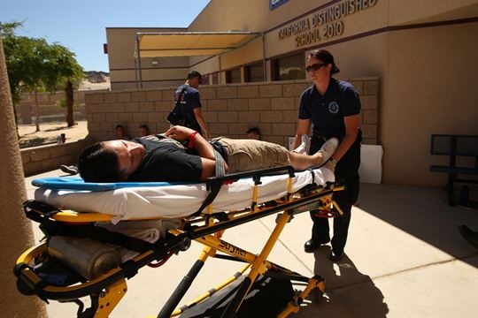 Becky Marx, a reserve emergency medical technician, transports a role player to an ambulance during an active shooter exercise at Marine Corps Air Ground Combat Center, Twentynine Palms, California. The Marine Corps is the first service to standardize E911 capabilities. The Consolidated Emergency Response Systems Program is implementing a product suite used across the nation by emergency dispatchers to locate the caller’s location on a graphical display by GPS, thus increasing response time. U.S. Marine Corps photo by Cpl. Charles Santamaria 