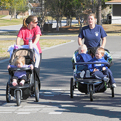 Two mothers walking with three children in strollers