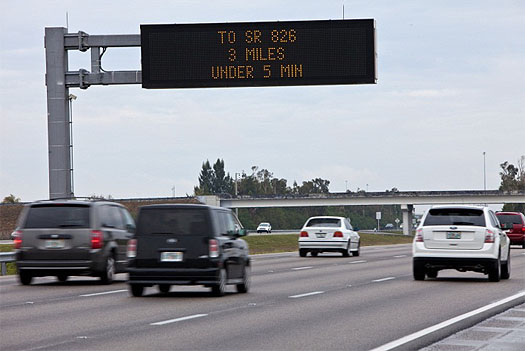 This is a photo of vehicles on a multi-lane highway passing under a dynamic message sign. The sign displays the message: To SR 826, 3 Miles, Under 5 Min.