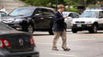 A man crosses in front of several cars while looking at his cell phone.