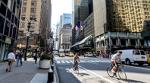 Pedestrians, cyclists, and cars travel through a dense urban area.