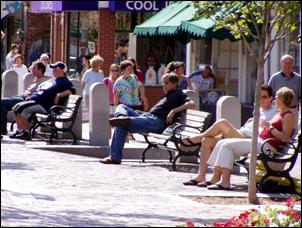 Photo. Image of people sitting in benches along a sidewalk.