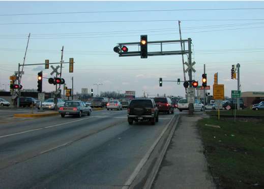 Figure 50. Pre-Signal Mounted on Railroad Cantilever, Rollins Road and State Route 83 at Wisconsin Central, Round Lake, Illinois. Image of cars crossing through intersection with cantilever, flashing signals.