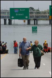 Photo of people near a flooded highway section. An Interstate sign in the background of a nearly flooded bridge points to 610 East, SLidell.