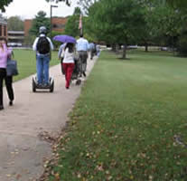 Back view of a Segway rider shares the roadway with pedestrians and a bicyclist.