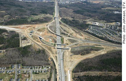 This aerial photograph, shot in April 2013, shows construction of the I–85 and I–485 turbine interchange near Charlotte, NC, one of three major projects underway in the region. Traffic on I–85 is moving through the center of the picture, while construction on the final leg of I–485 is shown on the left. Traffic on the right is merging from the existing portion of I–485 to I–85 north and south.