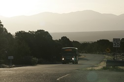 A photo of a transit vehicle driving through mountainous rural terrain.