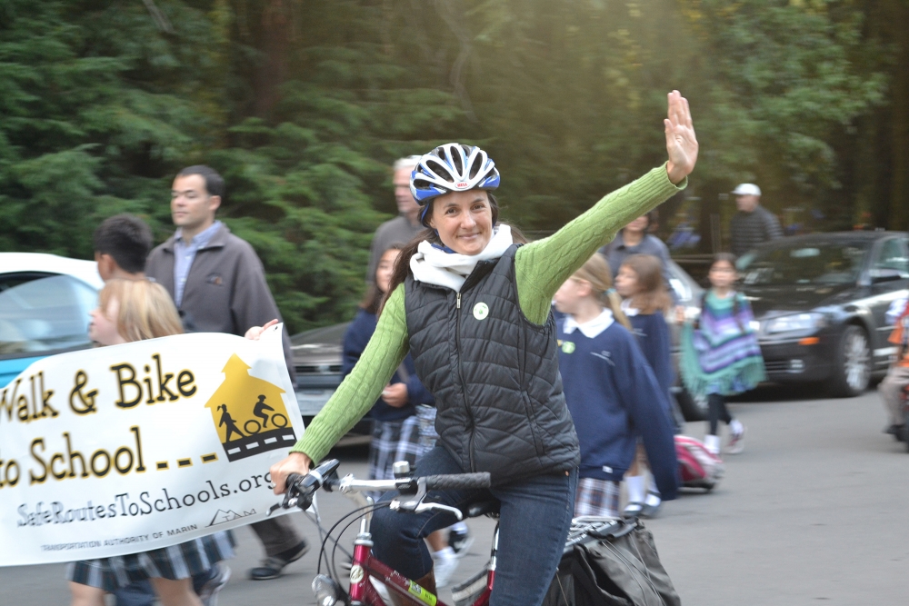 Deb Hubsmith waves to the camera while riding on her bike.