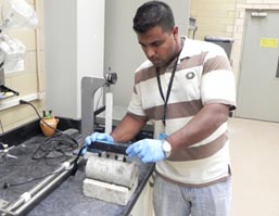 This image shows a research engineer in a laboratory. The engineer is reading the electrical resistance of a concrete cylinder by using a four-point Wenner probe.