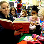 Picture of a teacher reading a book to a group of very young children in a classroom