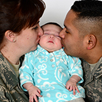 A father and mother in uniform, holding a tiny baby between them 