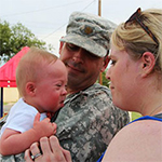 Service member holding baby next to spouse