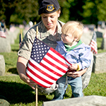 Service member with child placing flag at grave site 