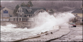Photograph of a storm surge overtopping a road with a car along a coast.