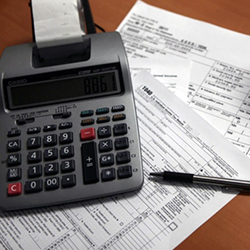 Tax documents, a calculator, pen and coffee mug on a table