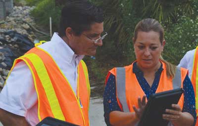 Photo. These project stakeholders wearing safety vests are reviewing information on a mobile device.