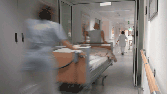 Two medical professionals rush a patient down a hospital hallway.