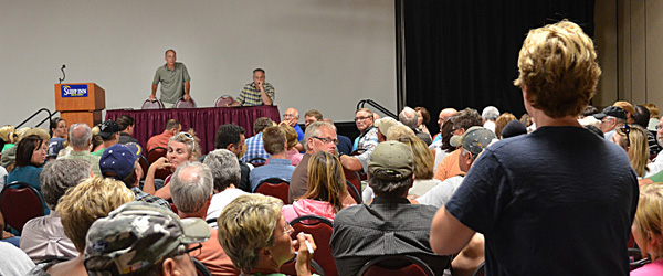 Image of man raising his had at a town hall meeting