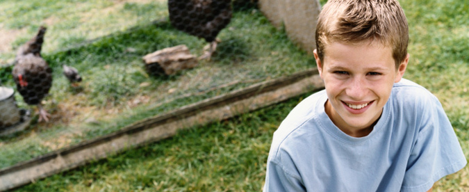 A boy stands in front of domestic poultry (chickens).